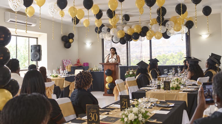 Salle de remise de diplômes décorée de ballons noirs et or.